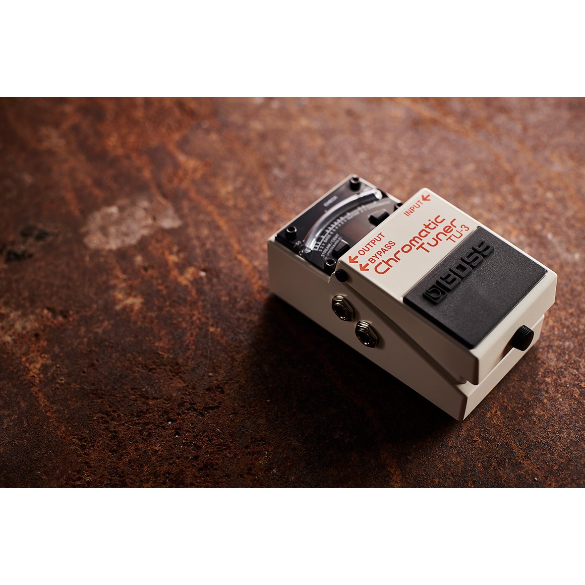 Pedal Tuner BOSS TU-3 Chromatic Tuner – đặt trên mặt gỗ, nhìn nghiêng thấy cạnh trái với 2 jack OUTPUT và BYPASS