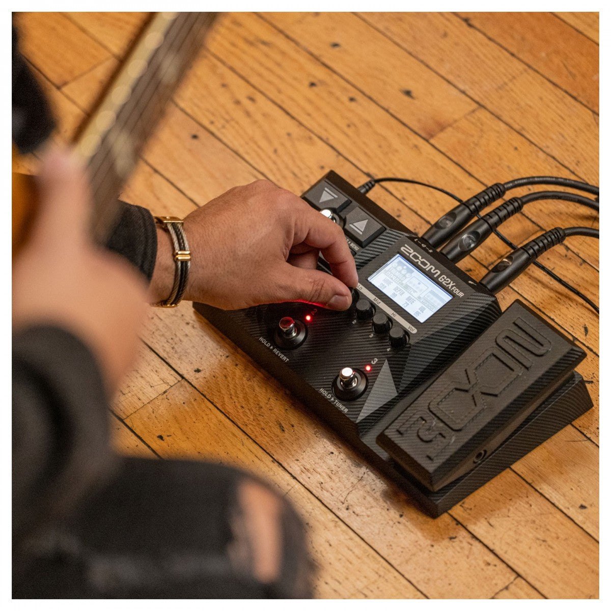 Phơ Tổng Zoom G2X FOUR – tay người chơi đang chỉnh núm, đặt cạnh đàn guitar